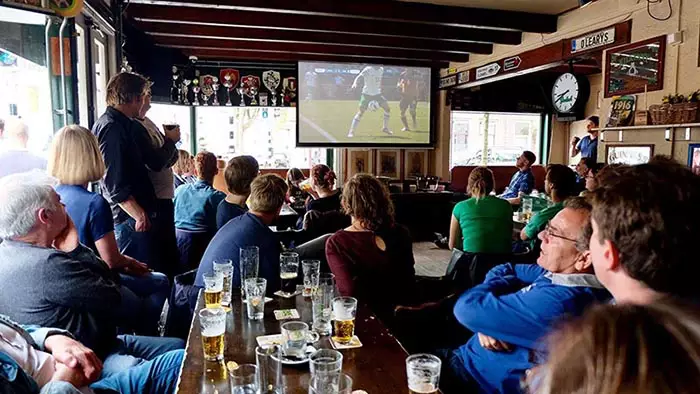 People sitting in O'Leary's pub drinking and watching a sports match